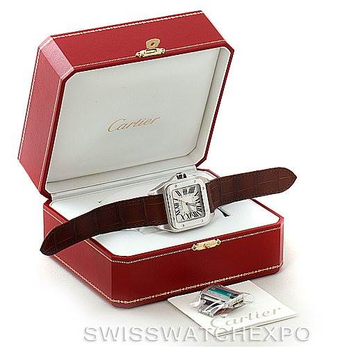 The image shows a Cartier Santos W20073X8 Men
s Stainless Steel Silver Dial W20073X8 Men
s Stainless Steel Silver Dial model watch in its open red box, with an additional strap and booklet placed beside it.