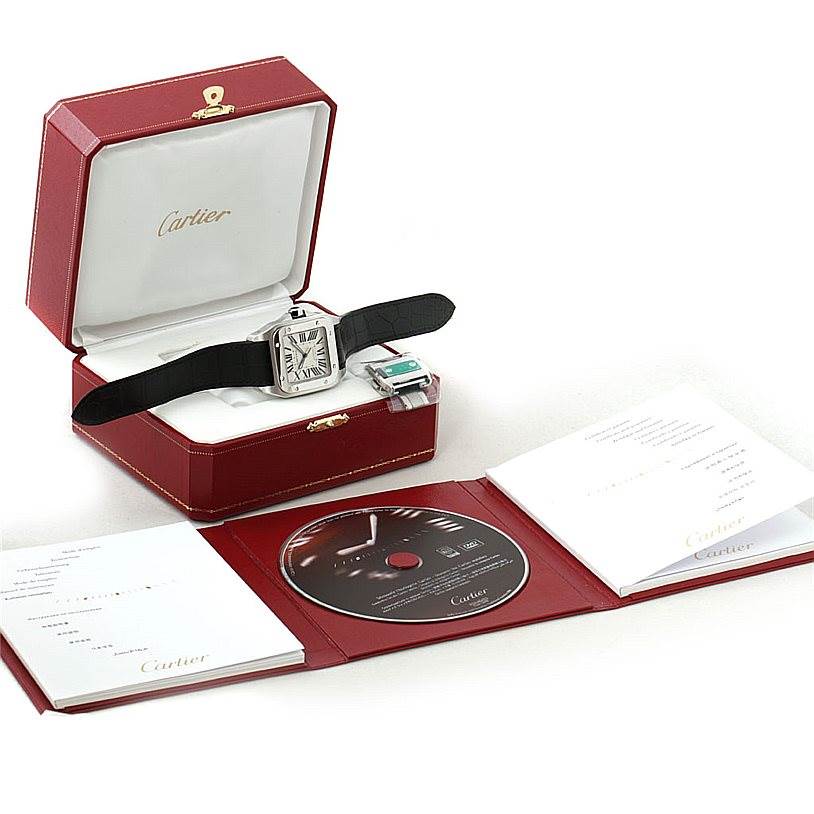 The image shows a Cartier Santos W20073X8 Men
s Stainless Steel Silver Dial W20073X8 Men
s Stainless Steel Silver Dial watch in its case, accompanied by warranty papers and a CD, viewed from above.