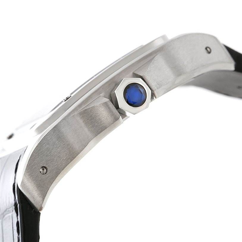 The image shows a side view of the Cartier Santos W20073X8 Men
s Stainless Steel Silver Dial W20073X8 Men
s Stainless Steel Silver Dial watch, highlighting the crown with a blue jewel and part of the case and strap.