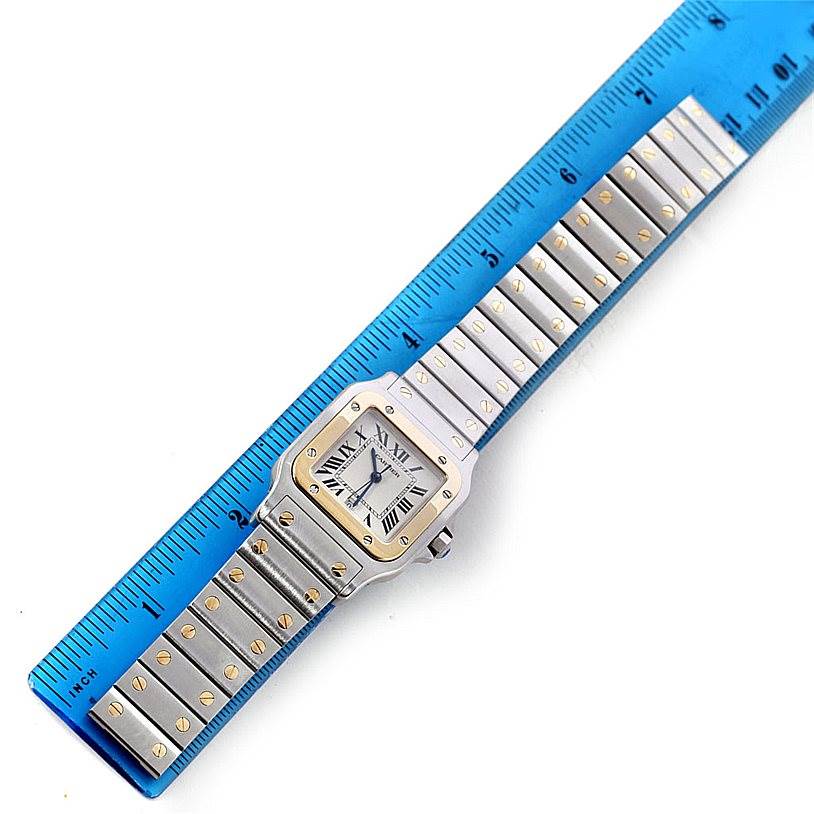 The image shows a Santos watch by Cartier, laid flat next to a blue ruler for size reference.