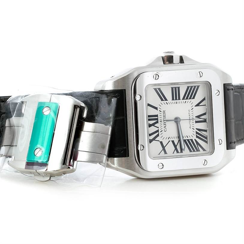 The image shows a Cartier Santos W20073X8 Men
s Stainless Steel Silver Dial W20073X8 Men
s Stainless Steel Silver Dial watch at an angle, highlighting its face, bezel, and parts of the strap with protective plastic.