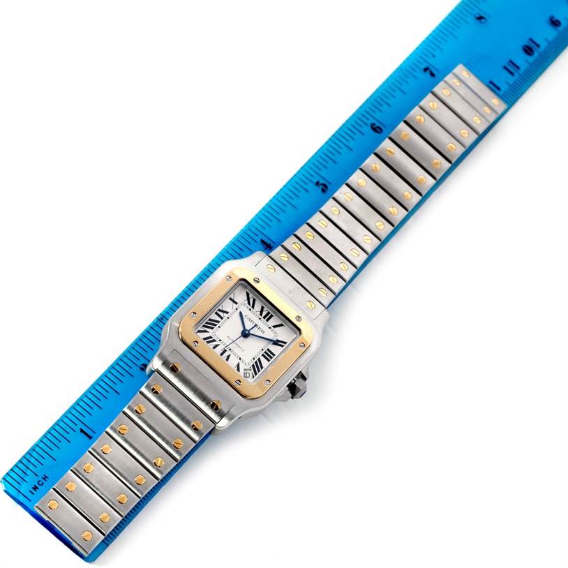 The image shows a top-down view of a Cartier Santos W20099C4 Men's Stainless Steel Silver Dial W20099C4 Men's Stainless Steel Silver Dial watch against a blue ruler, highlighting the watch face and bracelet.