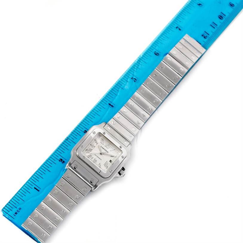 The Cartier Santos W20055D6 Men's Stainless Steel Silver Dial W20055D6 Men's Stainless Steel Silver Dial watch is laid flat with its face and full bracelet visible alongside a blue ruler for scale.