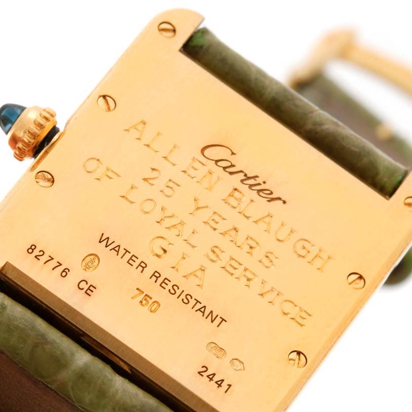 The image shows the engraved back case of the Tank Louis model by Cartier, featuring inscriptions and the crown partially visible.