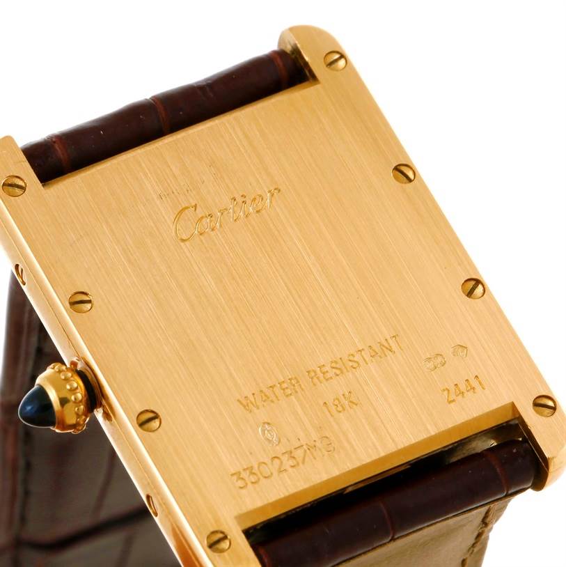 This image shows the back case of the Cartier Tank Louis W1529756 Men's Yellow Gold Silver Dial W1529756 Men's Yellow Gold Silver Dial model watch at an angle that reveals the engravings and brown leather strap.