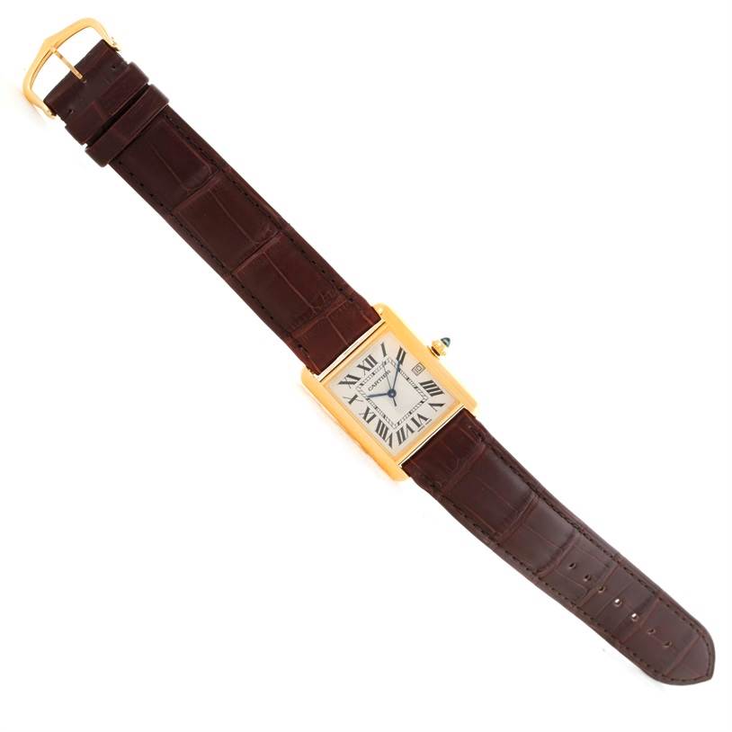The image shows an overhead view of the Tank Louis watch by Cartier, displaying its brown strap and rectangular face with Roman numerals.