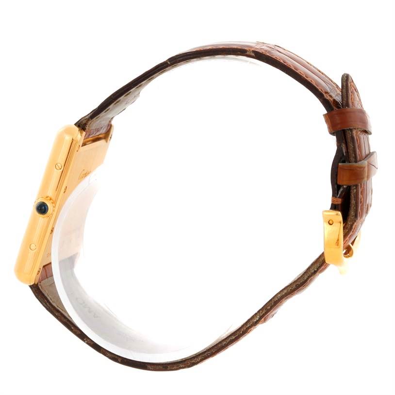 The image shows a side view of a Cartier Tank Louis Men's Yellow Gold Silver Dial Men's Yellow Gold Silver Dial watch, highlighting its gold rectangular case, blue stone crown, and brown leather strap.