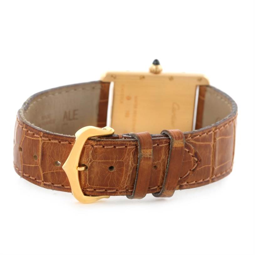 The image shows the back and clasp of a Tank Louis model watch by Cartier, focusing on its brown leather strap and gold buckle.