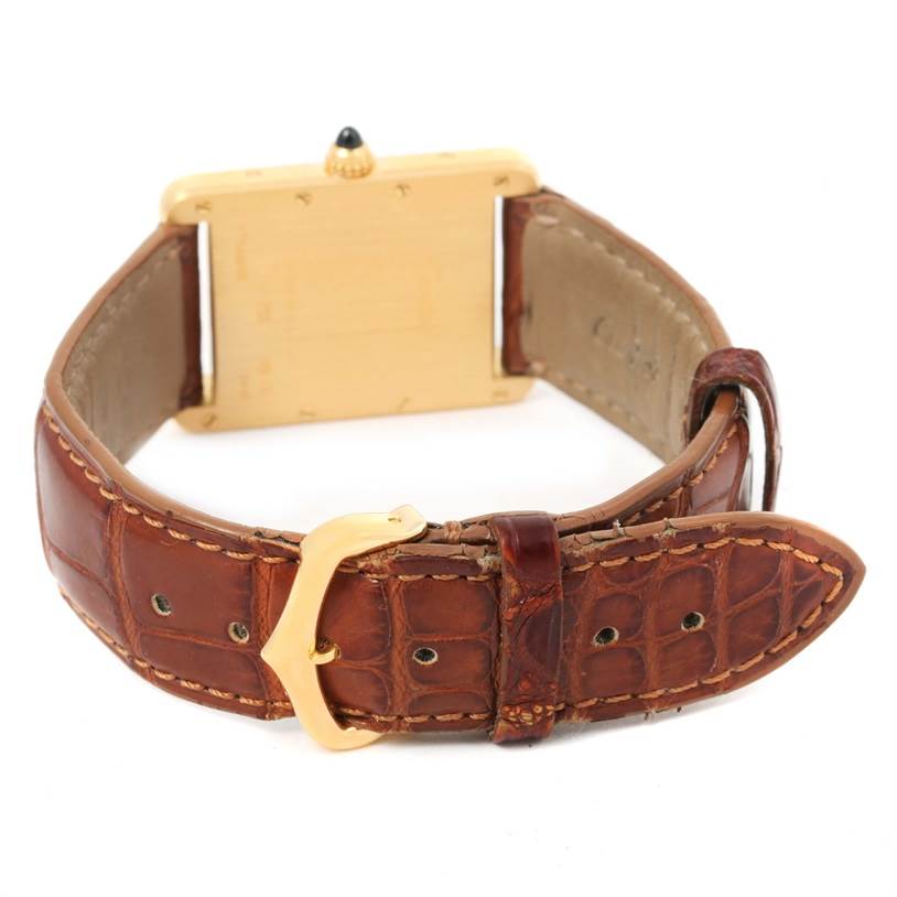 The image shows the Tank Louis model by Cartier from the back, highlighting the gold case, brown leather strap, and buckle.