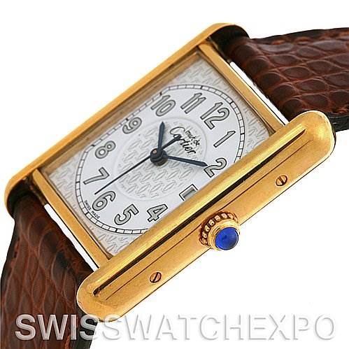 The image shows a close-up side angle of a Cartier Tank Louis Yellow Gold White Dial Yellow Gold White Dial watch, highlighting its gold case, crown with a blue gem, and brown leather strap.