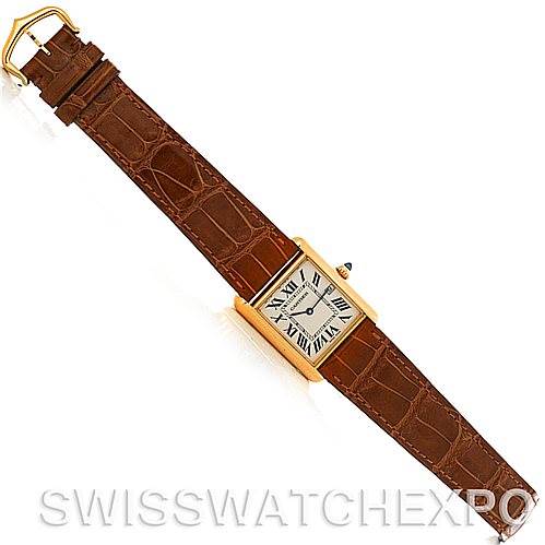 The Tank Louis Cartier watch is shown flat, displaying the face, brown leather strap, and gold buckle from an overhead angle.