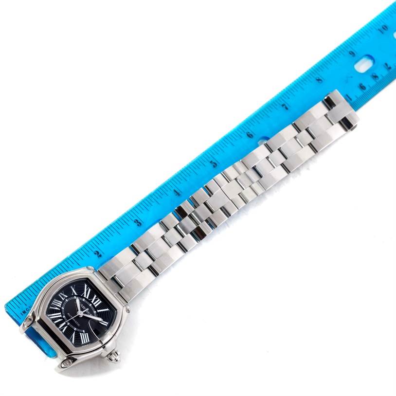 The image shows a Cartier Roadster W62041V3 Men
s Stainless Steel Black Dial W62041V3 Men
s Stainless Steel Black Dial watch, displaying its dial and stainless steel bracelet from an aerial angle, next to a ruler.