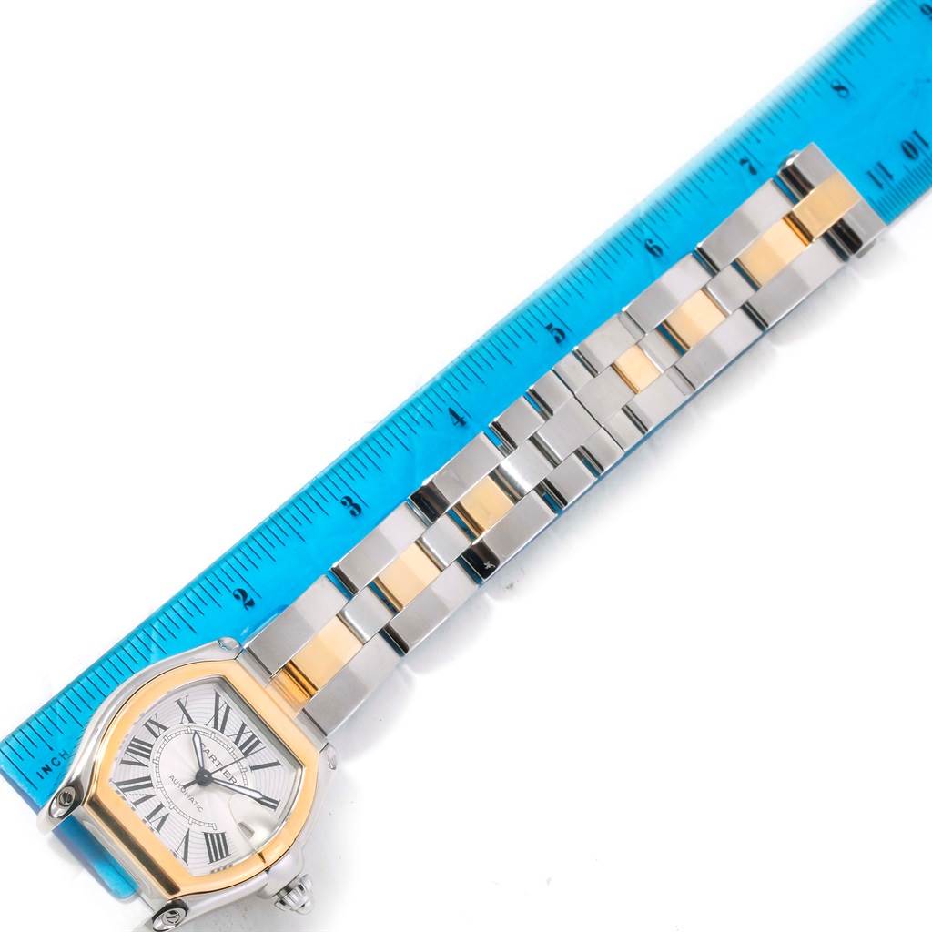 This image shows the Cartier Roadster W62031Y4 Men's Steel and Gold (two tone) Silver Dial W62031Y4 Men's Steel and Gold (two tone) Silver Dial watch face and metal bracelet alongside a blue ruler for measurement.