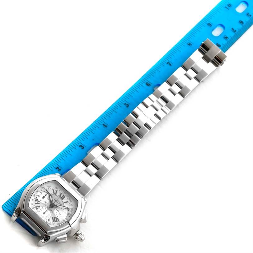 The image shows a top-down view of a Cartier Roadster W62006X6 Men's Stainless Steel Silver Dial W62006X6 Men's Stainless Steel Silver Dial watch with its linked metal bracelet and a blue ruler beside it.