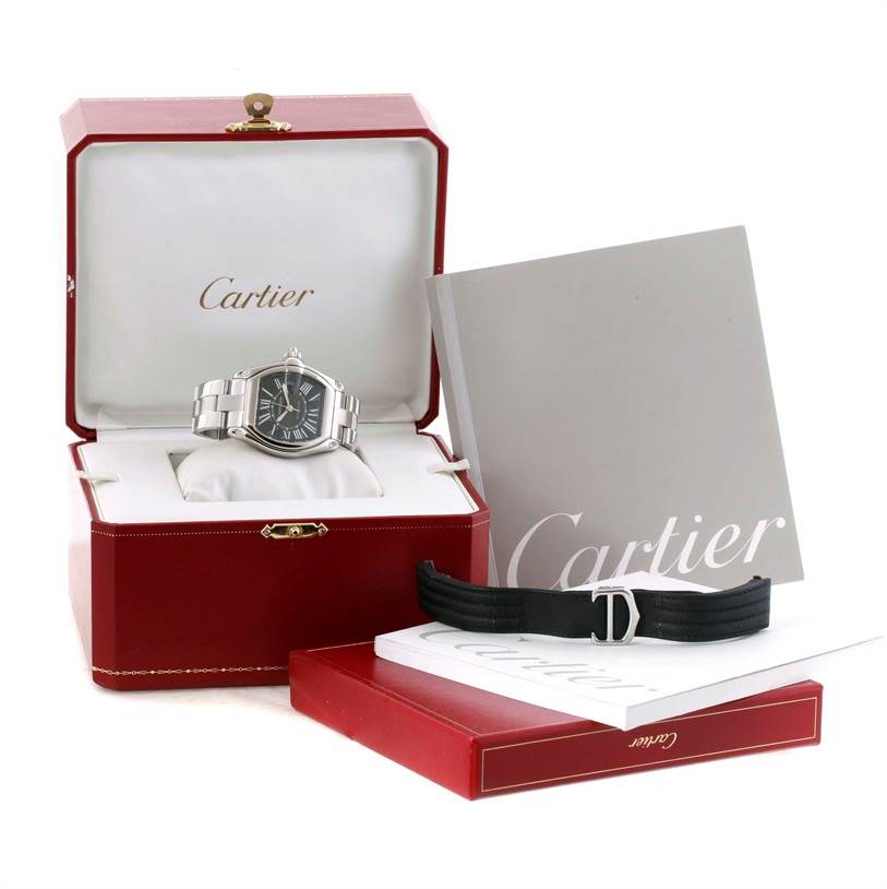 The image shows a Cartier Roadster W62041V3 Men's Stainless Steel Black Dial W62041V3 Men's Stainless Steel Black Dial watch in its open case with a booklet and an additional black strap.