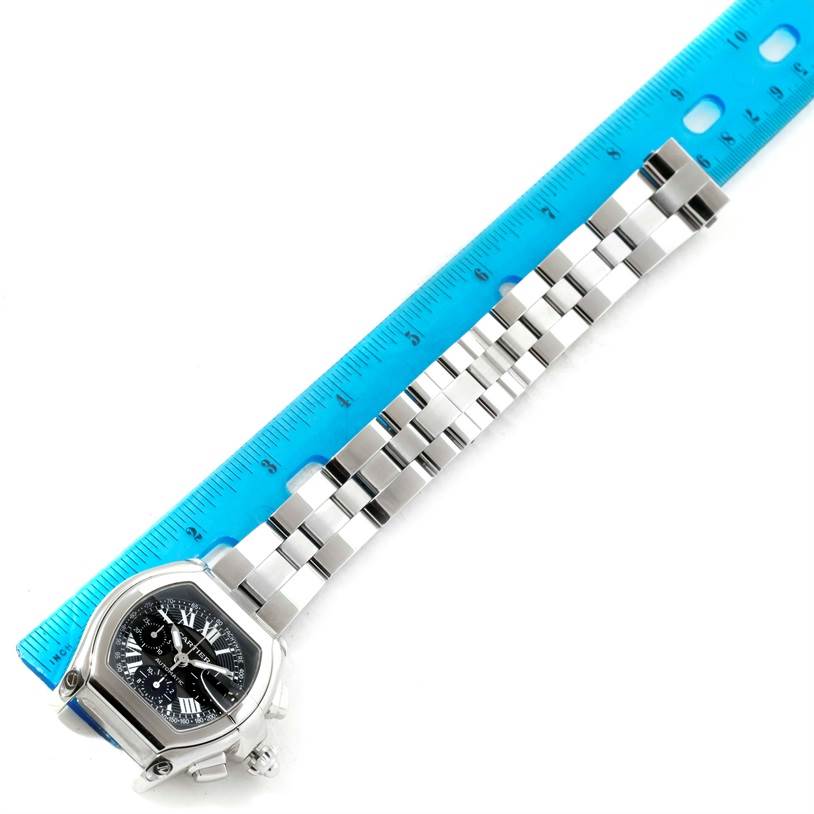 The Cartier Roadster W62007X6 Men's Stainless Steel Black Dial W62007X6 Men's Stainless Steel Black Dial watch is shown from an overhead angle, highlighting its face, bezel, and metal bracelet alongside a ruler.