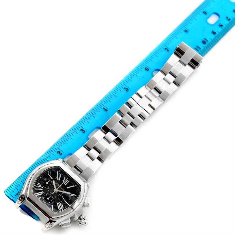 This image shows a Cartier Roadster W62020X6 Men's Stainless Steel Black Dial W62020X6 Men's Stainless Steel Black Dial watch face and its metal bracelet next to a blue ruler for measurement.
