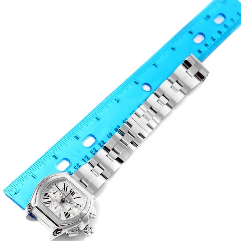 The Cartier Roadster W62019X6 Men's Stainless Steel Silver Dial W62019X6 Men's Stainless Steel Silver Dial watch is shown from a top-down angle alongside a blue ruler, highlighting the face, dial, and bracelet.