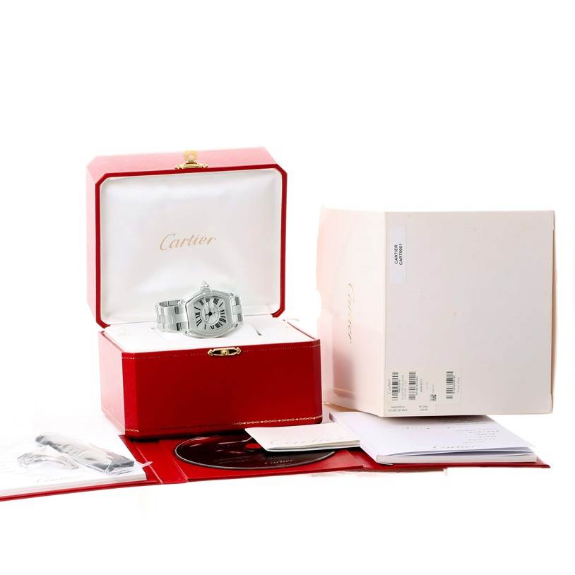 The Cartier Roadster W62025V3 Men's Stainless Steel Silver Dial W62025V3 Men's Stainless Steel Silver Dial watch is shown front-on in its open red box, with additional accessories and packaging displayed nearby.