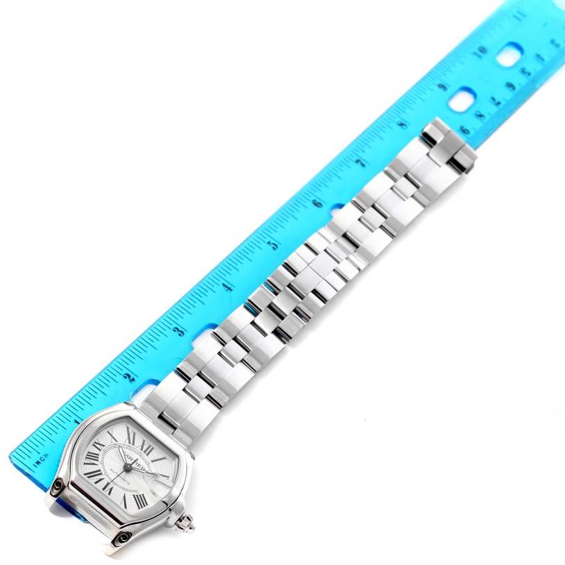 The Cartier Roadster W62025V3 Men's Stainless Steel Silver Dial W62025V3 Men's Stainless Steel Silver Dial watch is displayed laid flat with its bracelet and face visible, adjacent to a blue ruler.