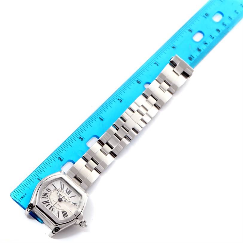 The Cartier Roadster W62025V3 Men's Stainless Steel Silver Dial W62025V3 Men's Stainless Steel Silver Dial watch is shown flat with its face and bracelet next to a blue ruler for scale.