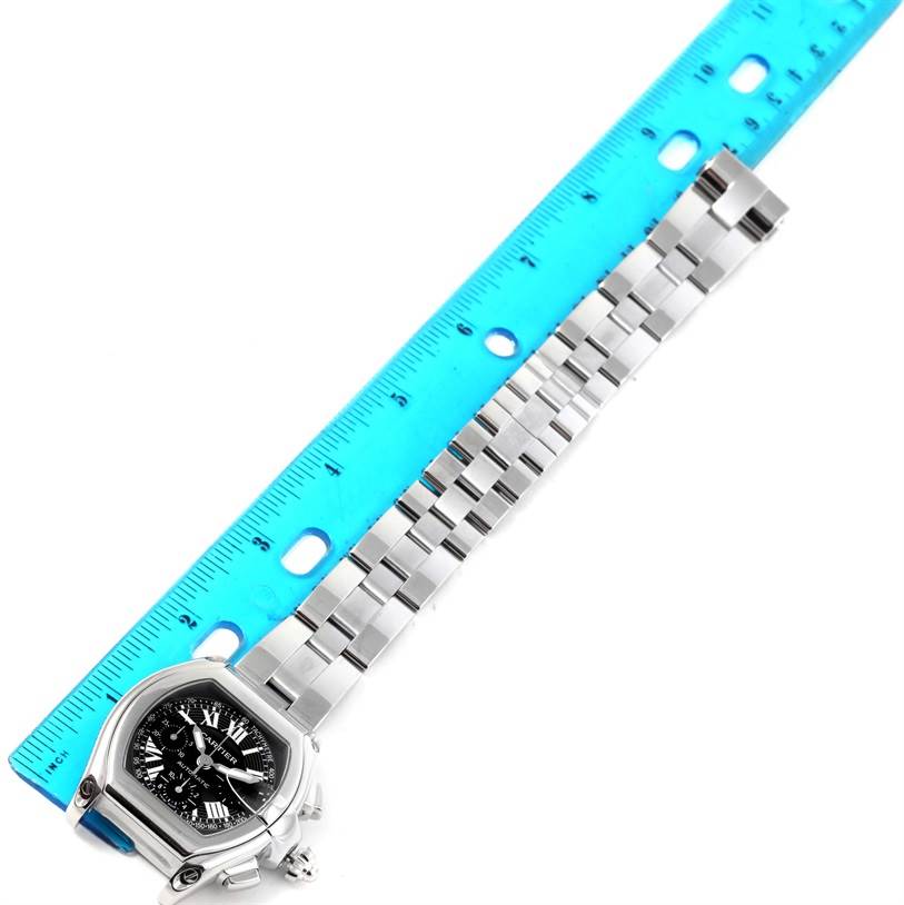 The image shows a top-down view of a Cartier Roadster W62007X6 Men's Stainless Steel Black Dial W62007X6 Men's Stainless Steel Black Dial watch including the face, crown, and metal bracelet aligned with a blue ruler.