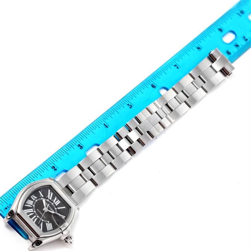 The image shows a Cartier Roadster W62041V3 Men
s Stainless Steel Black Dial W62041V3 Men
s Stainless Steel Black Dial watch with a focus on the strap next to a blue ruler for measurement.
