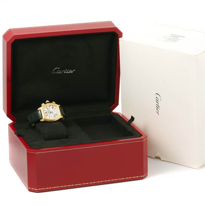 The Cartier Roadster W62021Y2 Men's Yellow Gold Silver Dial W62021Y2 Men's Yellow Gold Silver Dial watch is shown at an angle placed inside its red box, which is open next to a white Cartier box.