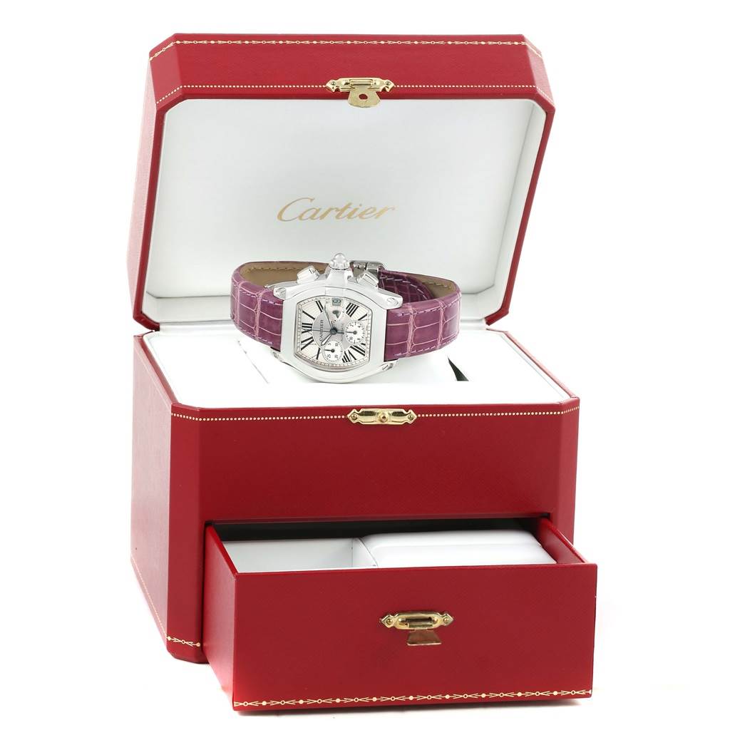 The Cartier Roadster W62019X6 Men's Stainless Steel Silver Dial W62019X6 Men's Stainless Steel Silver Dial watch is displayed at a front angle in an open red box with a purple leather strap.