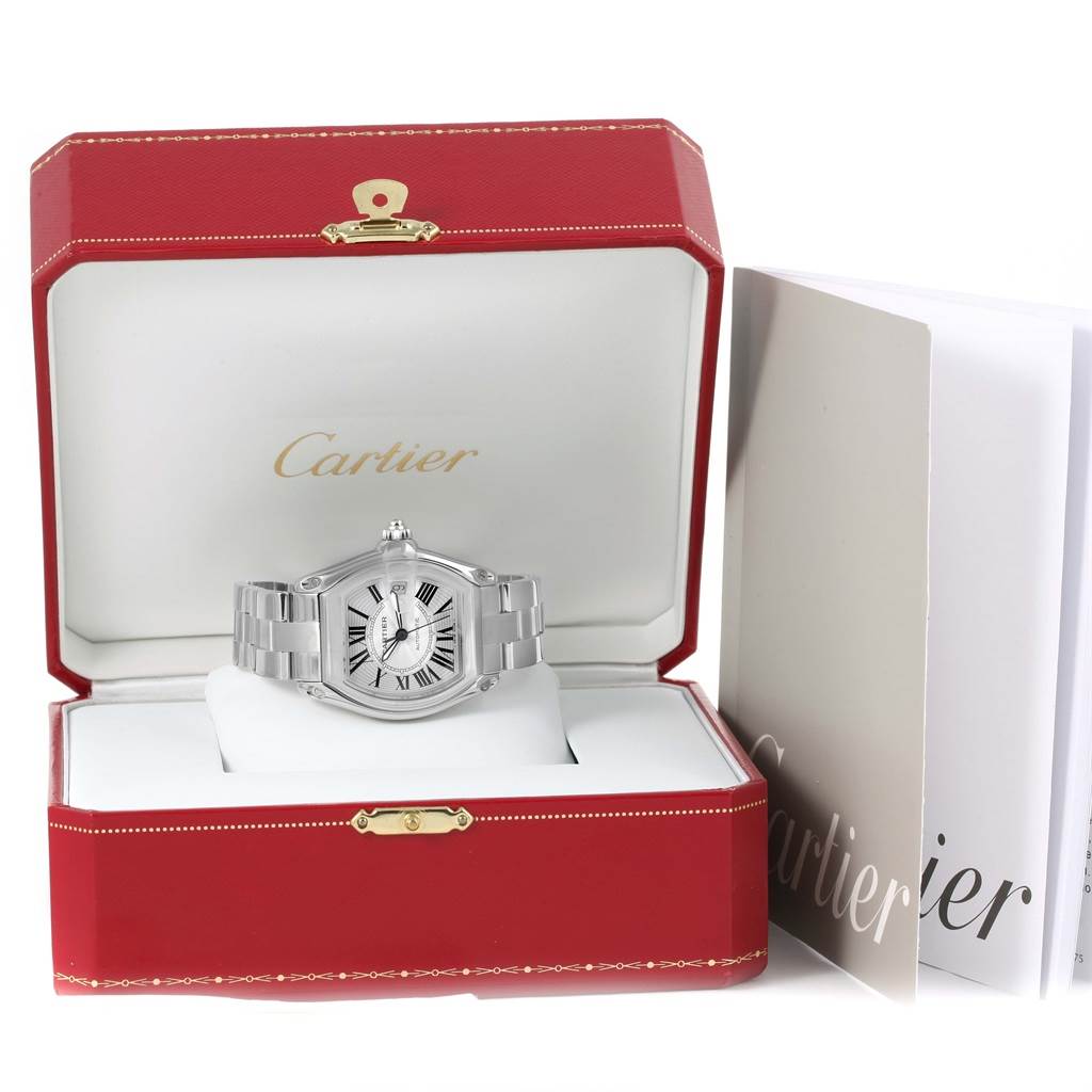 The Cartier Roadster W62025V3 Men
s Stainless Steel Silver Dial W62025V3 Men
s Stainless Steel Silver Dial watch is displayed front-on inside a red Cartier box with accompanying documents on the right.