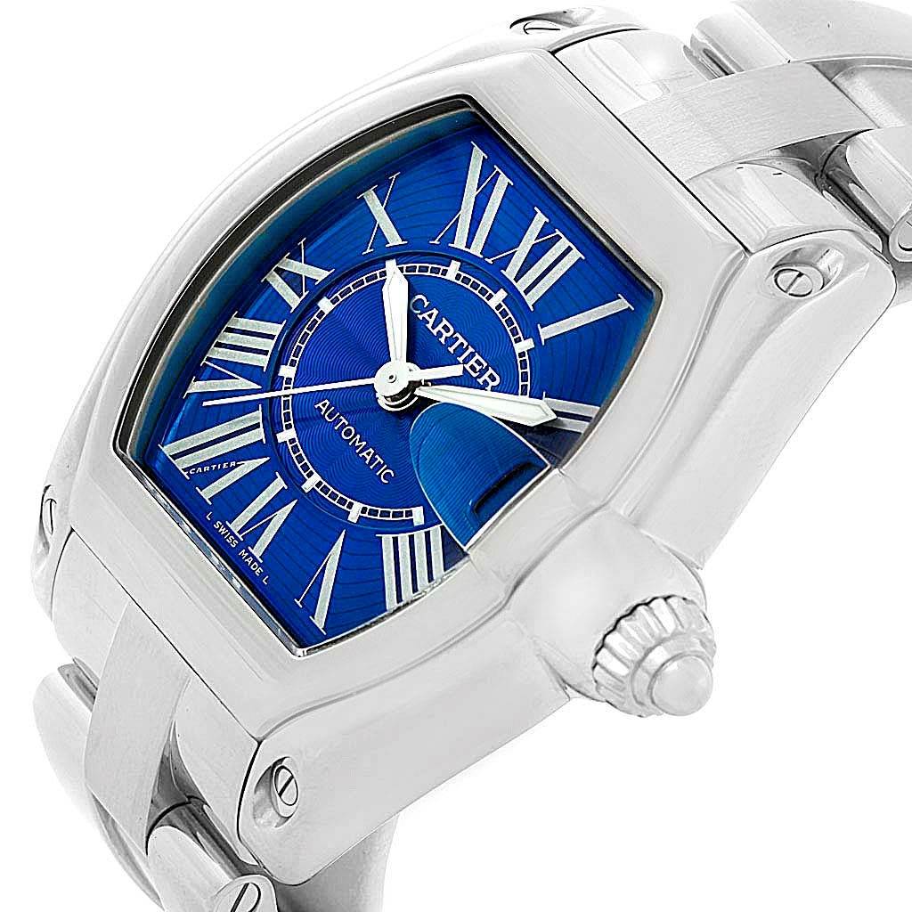 The image shows a close-up angled view of a Cartier Roadster W62048V3 Men
s Blue Dial W62048V3 Men
s Blue Dial watch, highlighting the blue dial, crown, and part of the bracelet.