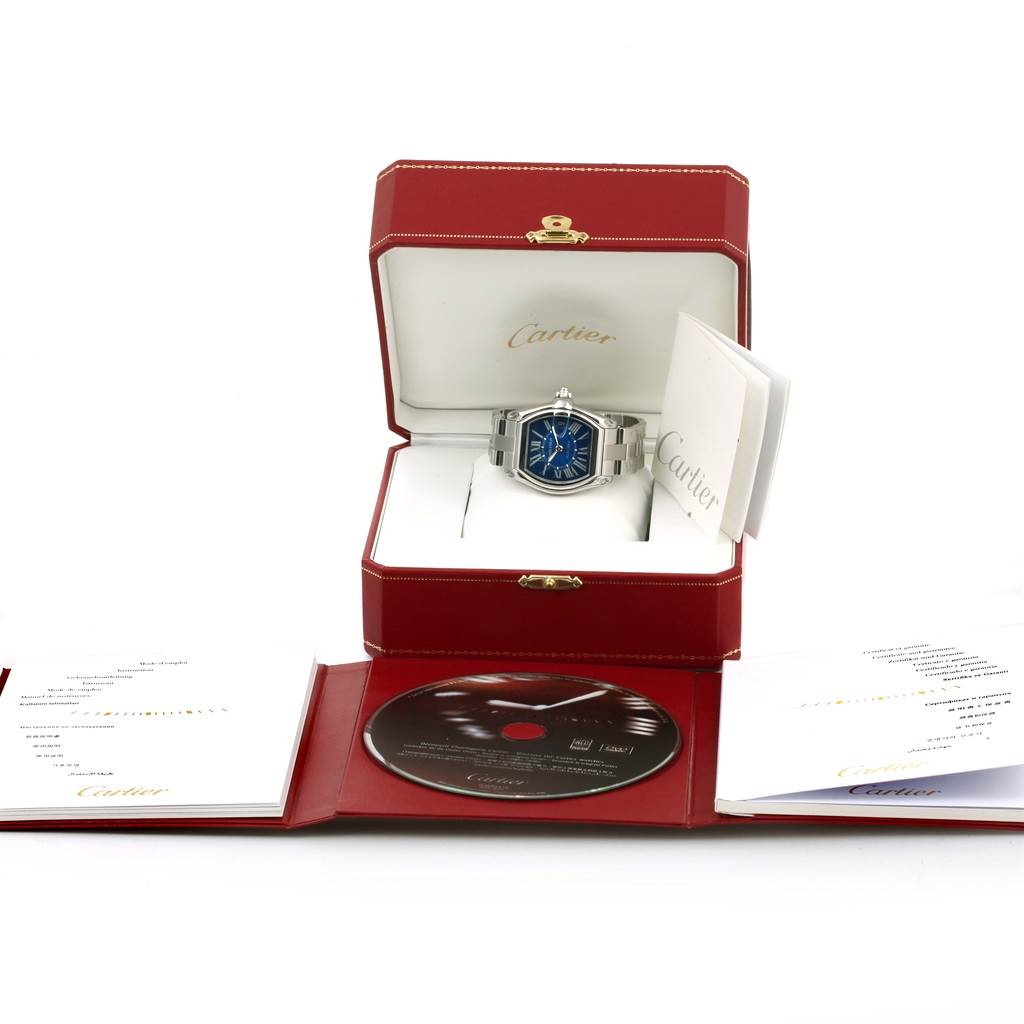 The image shows a Cartier Roadster W62048V3 Men
s Blue Dial W62048V3 Men
s Blue Dial watch in its open box, along with documents and a CD, viewed from the front.