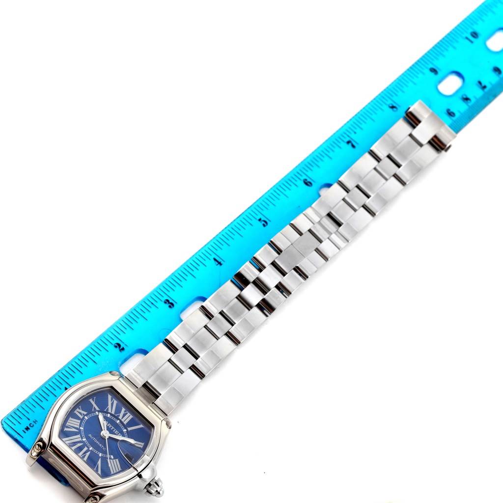 This image shows a Cartier Roadster W62048V3 Men
s Blue Dial W62048V3 Men
s Blue Dial watch laid flat with its length measured against a blue ruler.