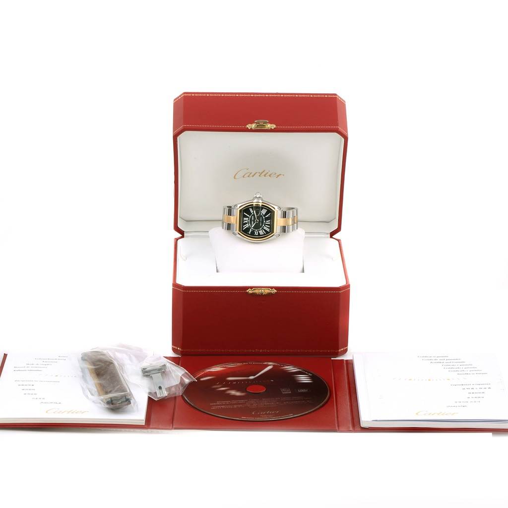 The image shows a Cartier Roadster W62031Y4 Men's Steel and Gold (two tone) Black Dial W62031Y4 Men's Steel and Gold (two tone) Black Dial watch in its box, along with its accessories including a manual, extra strap, and a CD.