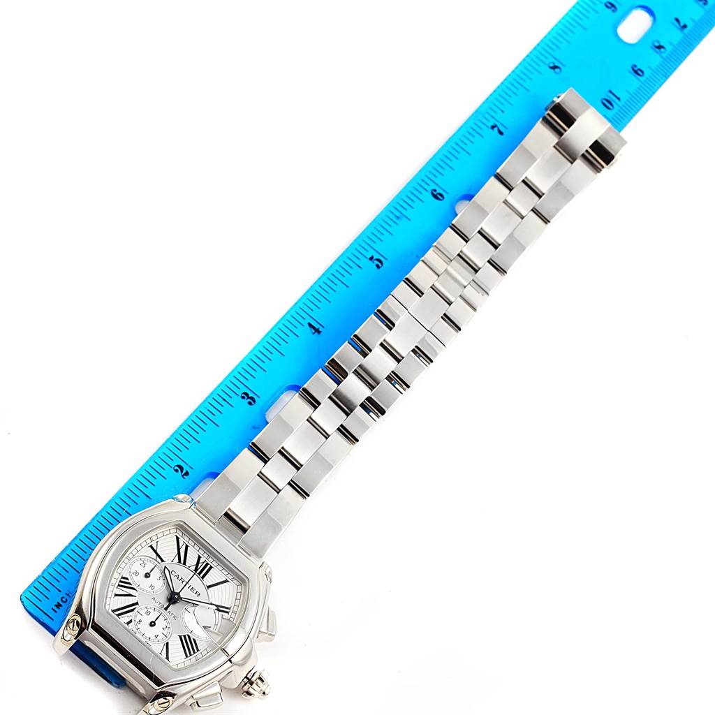 This image showcases a Cartier Roadster W62019X6 Men
s Stainless Steel Silver Dial W62019X6 Men
s Stainless Steel Silver Dial watch laid flat with its band extended next to a ruler.