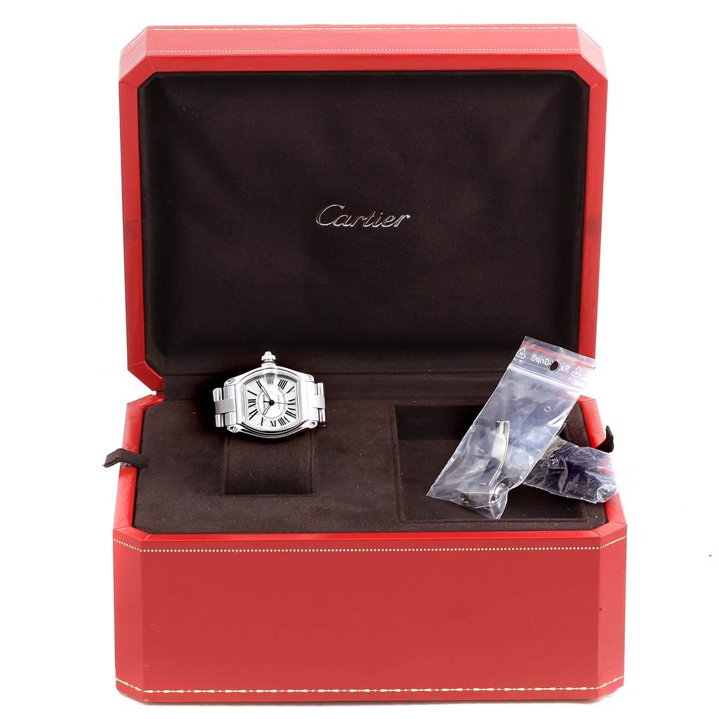 The image shows a Cartier Roadster W62025V3 Men
s Stainless Steel Silver Dial W62025V3 Men
s Stainless Steel Silver Dial watch and accessories at a side angle inside an open red presentation box with the Cartier logo.