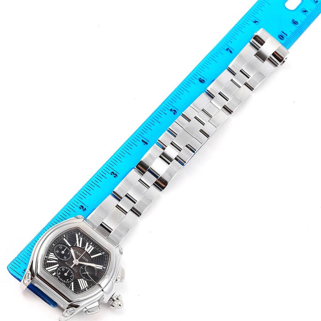 The image shows the Cartier Roadster W62020X6 Men
s Stainless Steel Black Dial W62020X6 Men
s Stainless Steel Black Dial watch face and full bracelet laid next to a blue ruler for measurement.