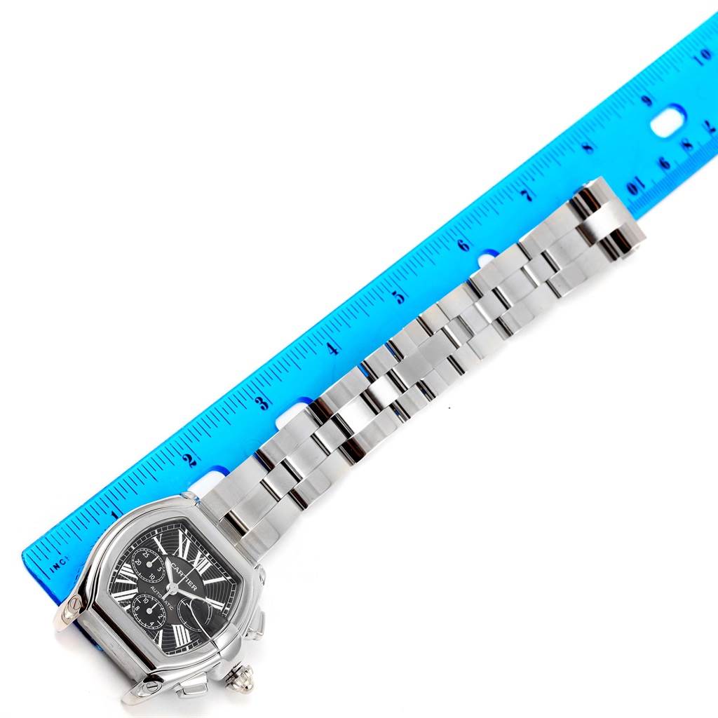 The Cartier Roadster W62020X6 Men's Stainless Steel Black Dial W62020X6 Men's Stainless Steel Black Dial watch is shown from above, displaying its face and metal bracelet alongside a blue ruler for scale.