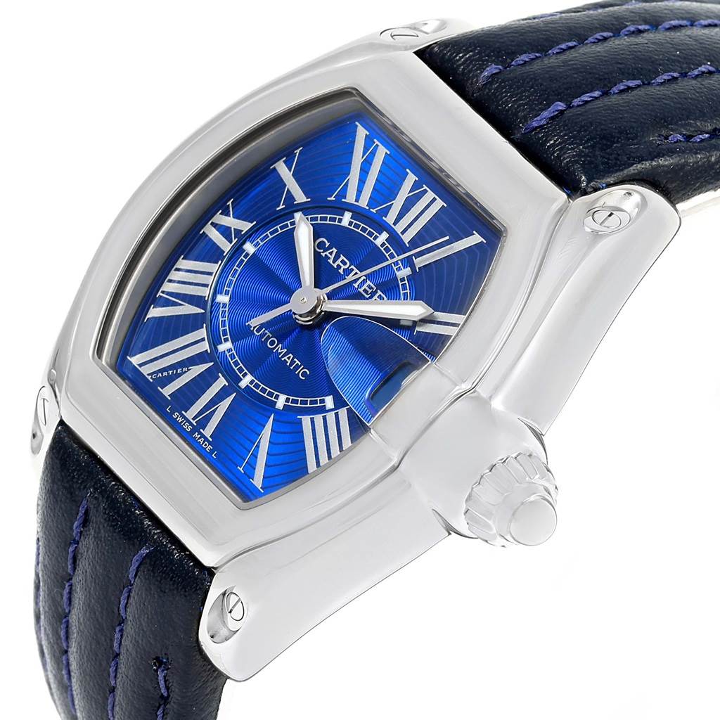 The image shows a Cartier Roadster W62048V3 Men's Stainless Steel Blue Dial W62048V3 Men's Stainless Steel Blue Dial watch at an angle highlighting its blue dial, Roman numerals, and side crown with a leather strap.