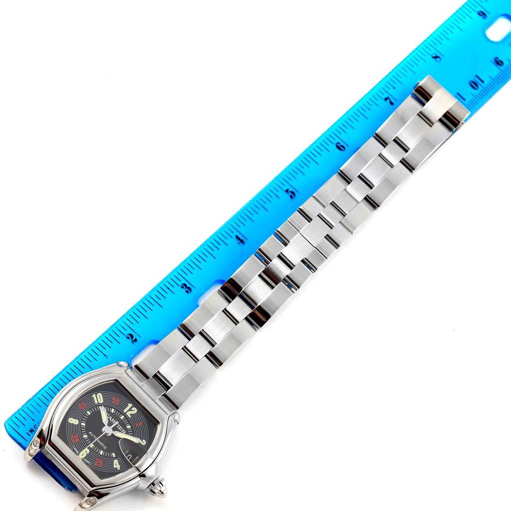 The image shows the Cartier Roadster W62002V3 Men's Stainless Steel Black Dial W62002V3 Men's Stainless Steel Black Dial watch laying flat next to a ruler, displaying its face and metal bracelet.