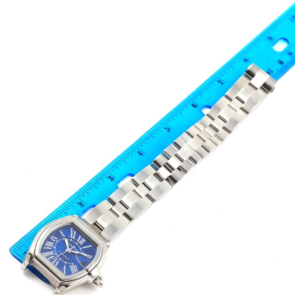 The Cartier Roadster W62048V3 Men's Stainless Steel Blue Dial W62048V3 Men's Stainless Steel Blue Dial watch is shown from an overhead angle, detailing its blue face and metal bracelet next to a blue ruler for size reference.