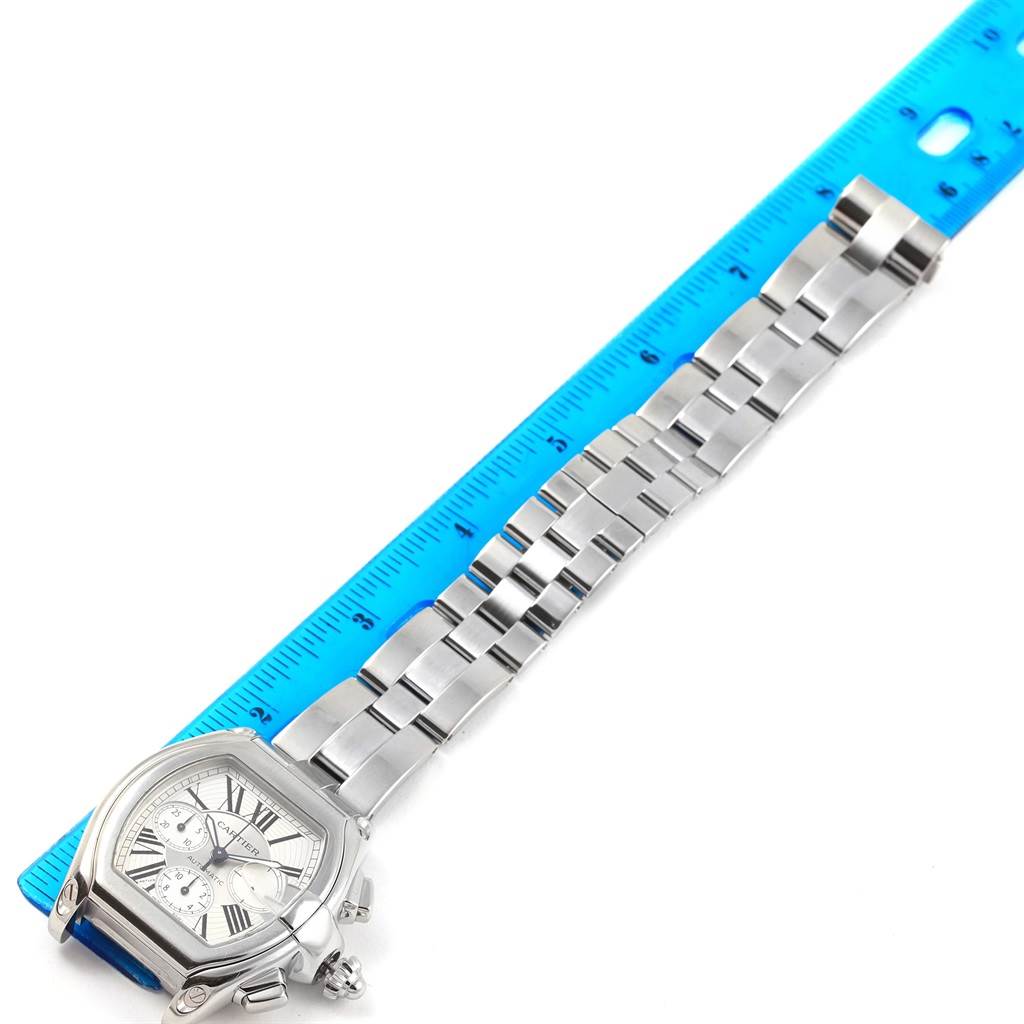 The Cartier Roadster W62019X6 Men's Stainless Steel Silver Dial W62019X6 Men's Stainless Steel Silver Dial watch is shown lying flat with a blue ruler, displaying the face and metallic bracelet.