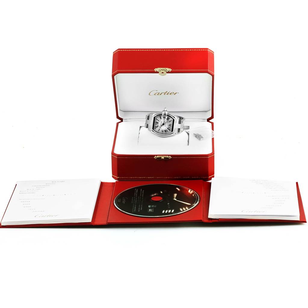 The image shows a Cartier Roadster W62025V3 Men's Stainless Steel Silver Dial W62025V3 Men's Stainless Steel Silver Dial watch in its open case, accompanied by booklets and a CD.