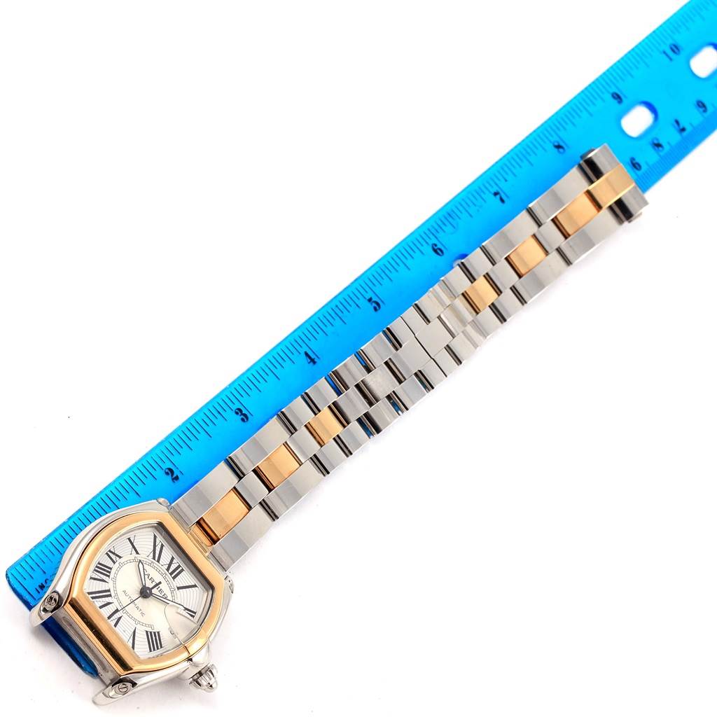 The image shows a top view of a Cartier Roadster W62031Y4 Men's Steel and Gold (two tone) Silver Dial W62031Y4 Men's Steel and Gold (two tone) Silver Dial watch with a two-tone metal bracelet alongside a blue ruler.