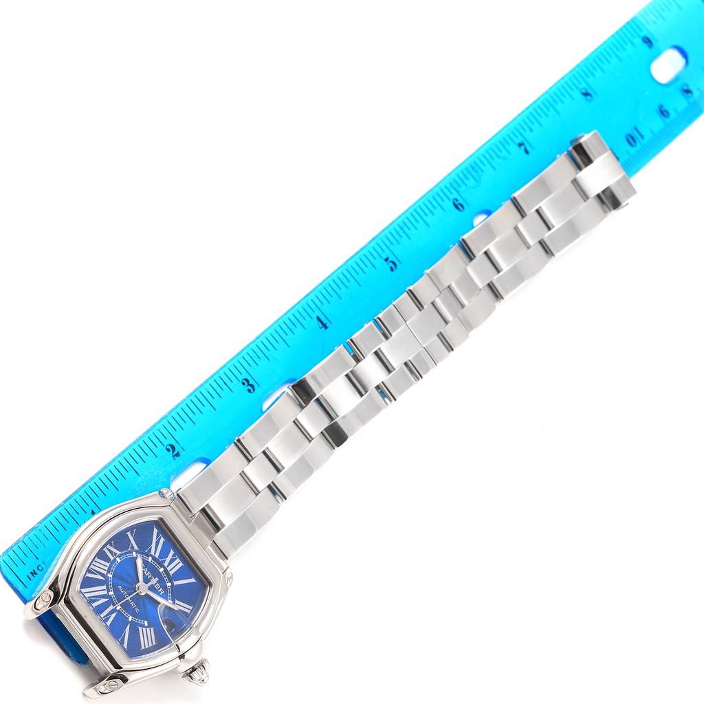 The Cartier Roadster W62048V3 Men's Stainless Steel Blue Dial W62048V3 Men's Stainless Steel Blue Dial watch is shown at an angle revealing its face, band, and a blue ruler for measurement.