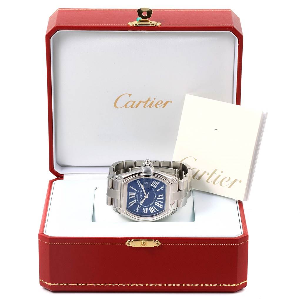 The Cartier Roadster W6206012 Men
s Stainless Steel Blue Dial W6206012 Men
s Stainless Steel Blue Dial watch is shown front-facing, placed inside an open Cartier box, with accompanying papers beside it.