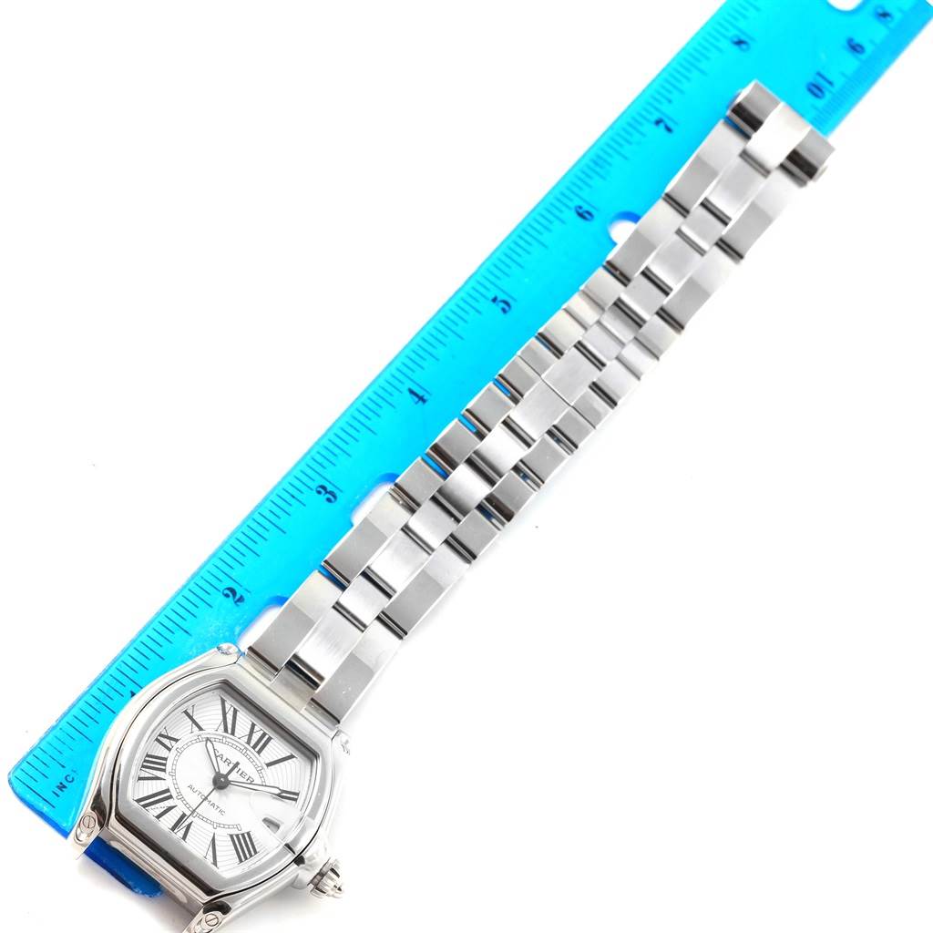 The image shows a Cartier Roadster W62025V3 Men's Stainless Steel Silver Dial W62025V3 Men's Stainless Steel Silver Dial watch with its face and metal bracelet laid next to a blue ruler.