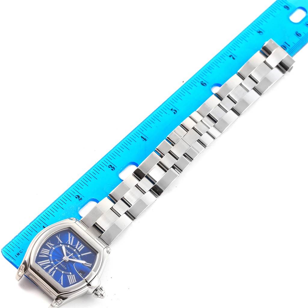 The image shows a top-down view of a Cartier Roadster W62048V3 Men's Stainless Steel Blue Dial W62048V3 Men's Stainless Steel Blue Dial watch next to a blue ruler, highlighting the face and part of the bracelet.