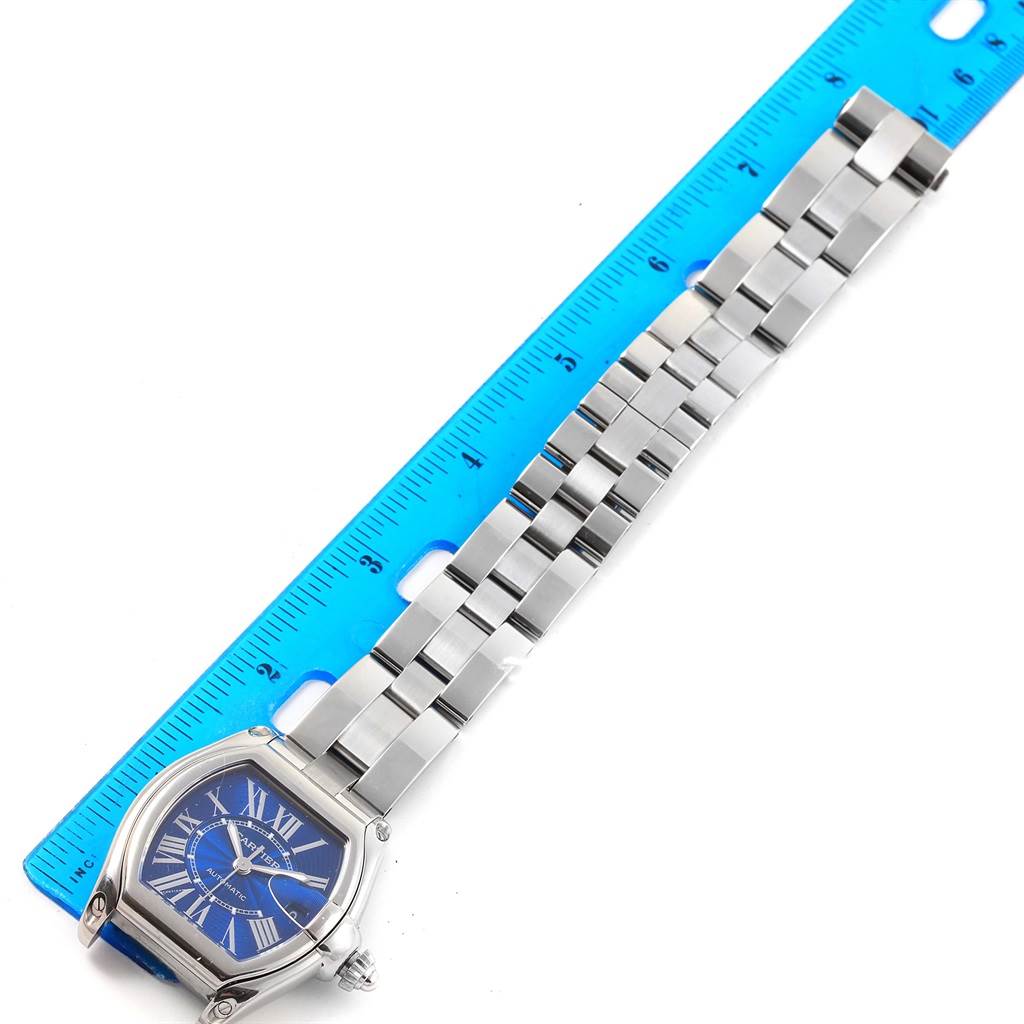 The Cartier Roadster W62048V3 Men's Stainless Steel Blue Dial W62048V3 Men's Stainless Steel Blue Dial watch is shown from an overhead angle, displaying the face, bracelet, and part of a blue ruler for scale.