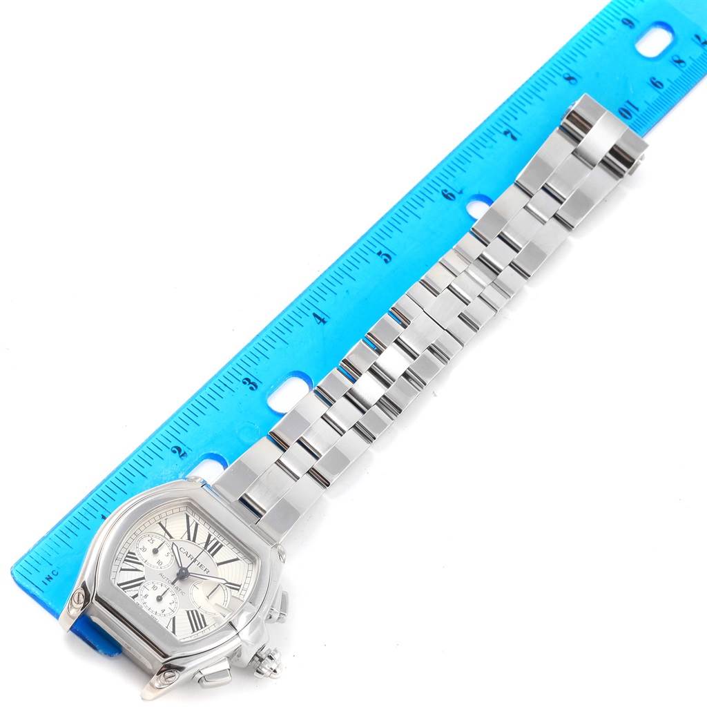The image shows a Cartier Roadster W62019X6 Men's Stainless Steel Silver Dial W62019X6 Men's Stainless Steel Silver Dial watch positioned next to a blue ruler, clearly displaying its face and metal bracelet.